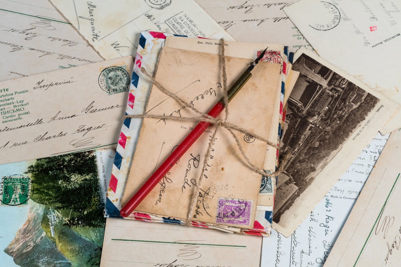 services-03 A collection of vintage postcards and envelopes tied with twine, featuring a pen and old stamps.